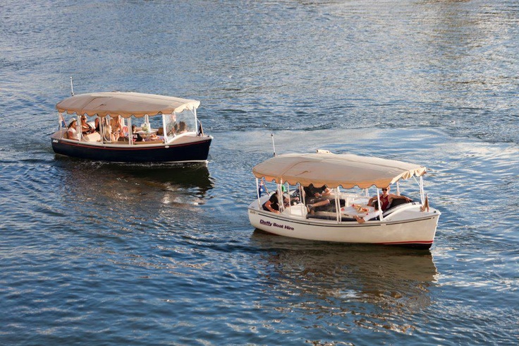 Two boats with beige canopies floating on water, with people on board, reflecting sunlight.