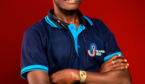 Young man with arms crossed, wearing a navy blue polo shirt with blue accents, standing against a red background.
