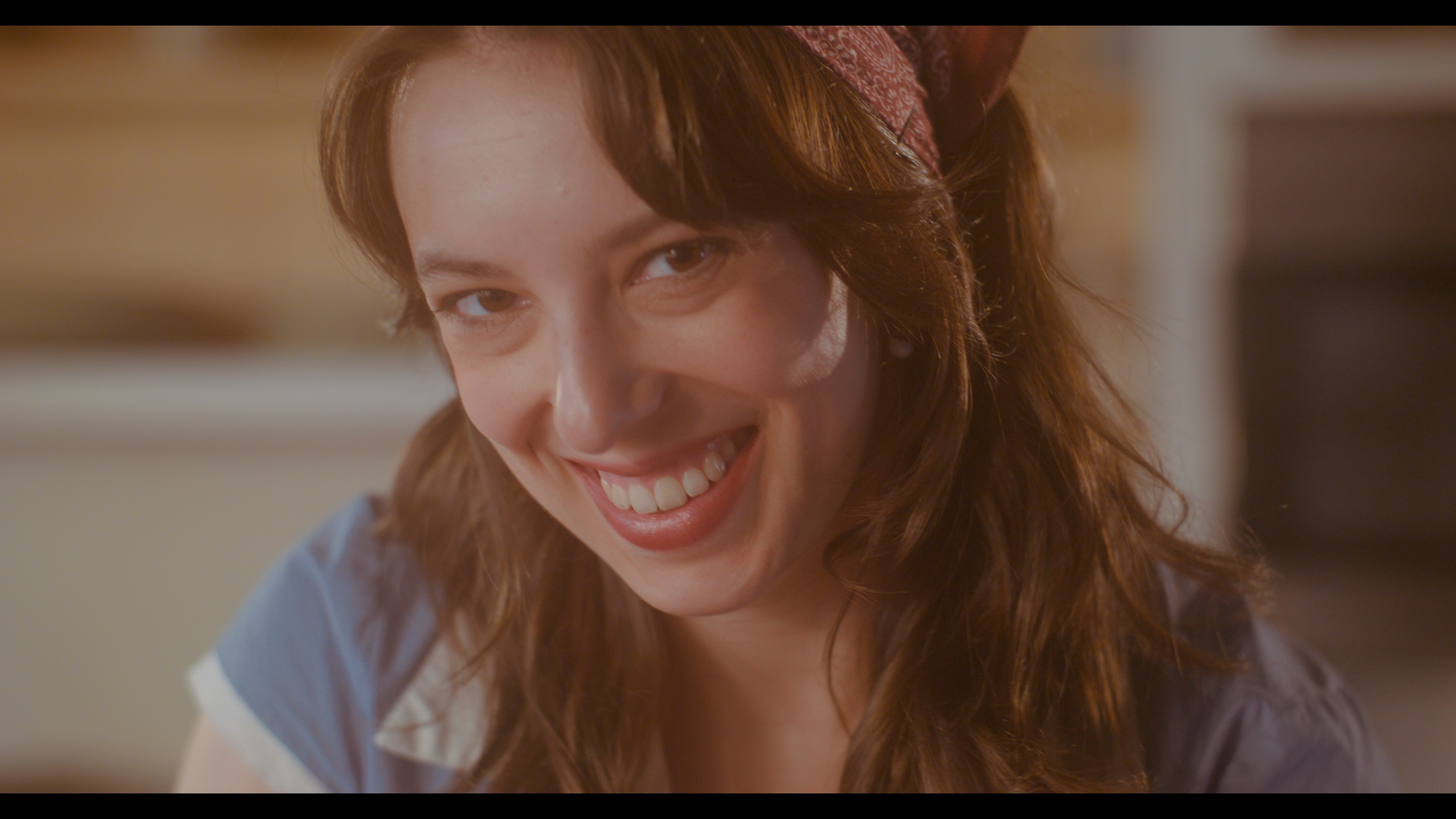 Smiling woman with brown hair and a headband, wearing a blue and white shirt, indoors.