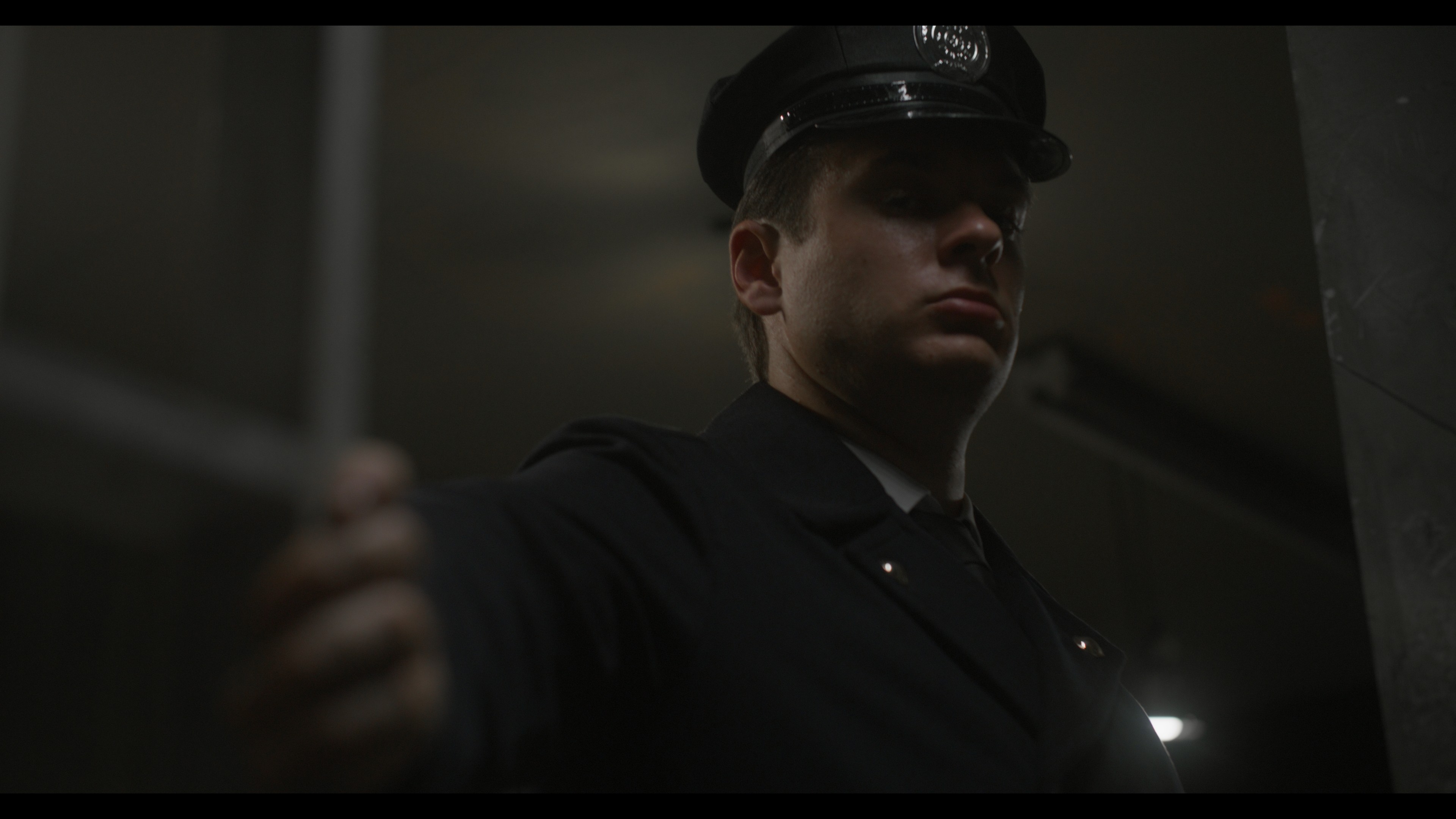 Person in police uniform with cap, in a dimly lit indoor setting.