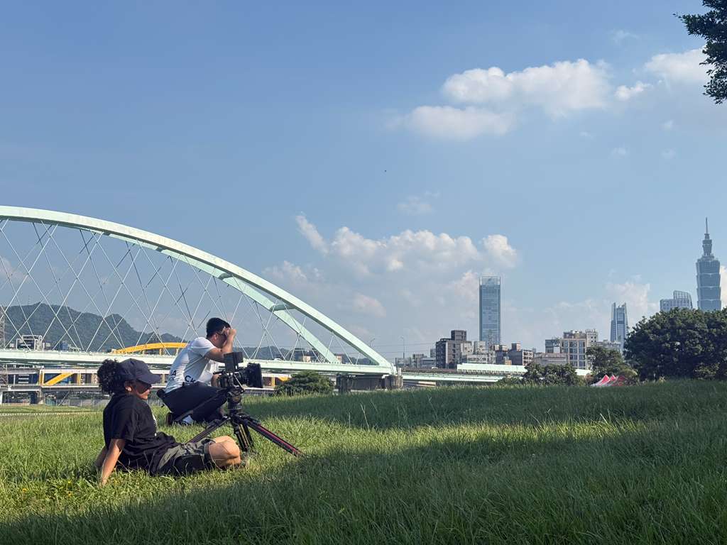 Two children playing on grass with a city skyline and a large white arch structure in the background.