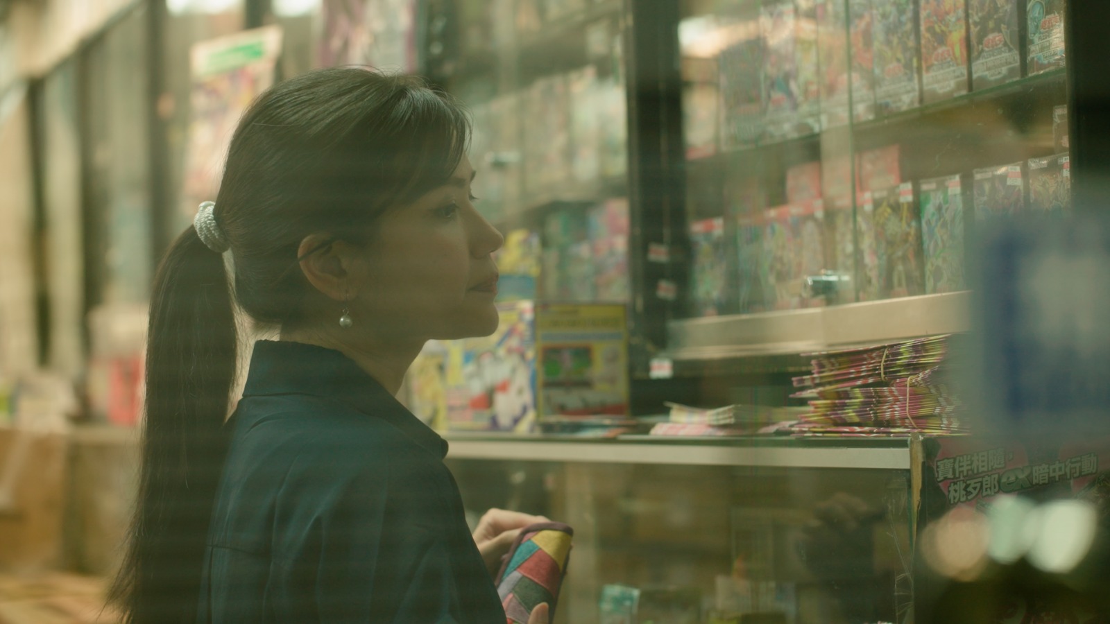 Woman with a ponytail shopping at a store, holding a phone, looking at shelves with products.
