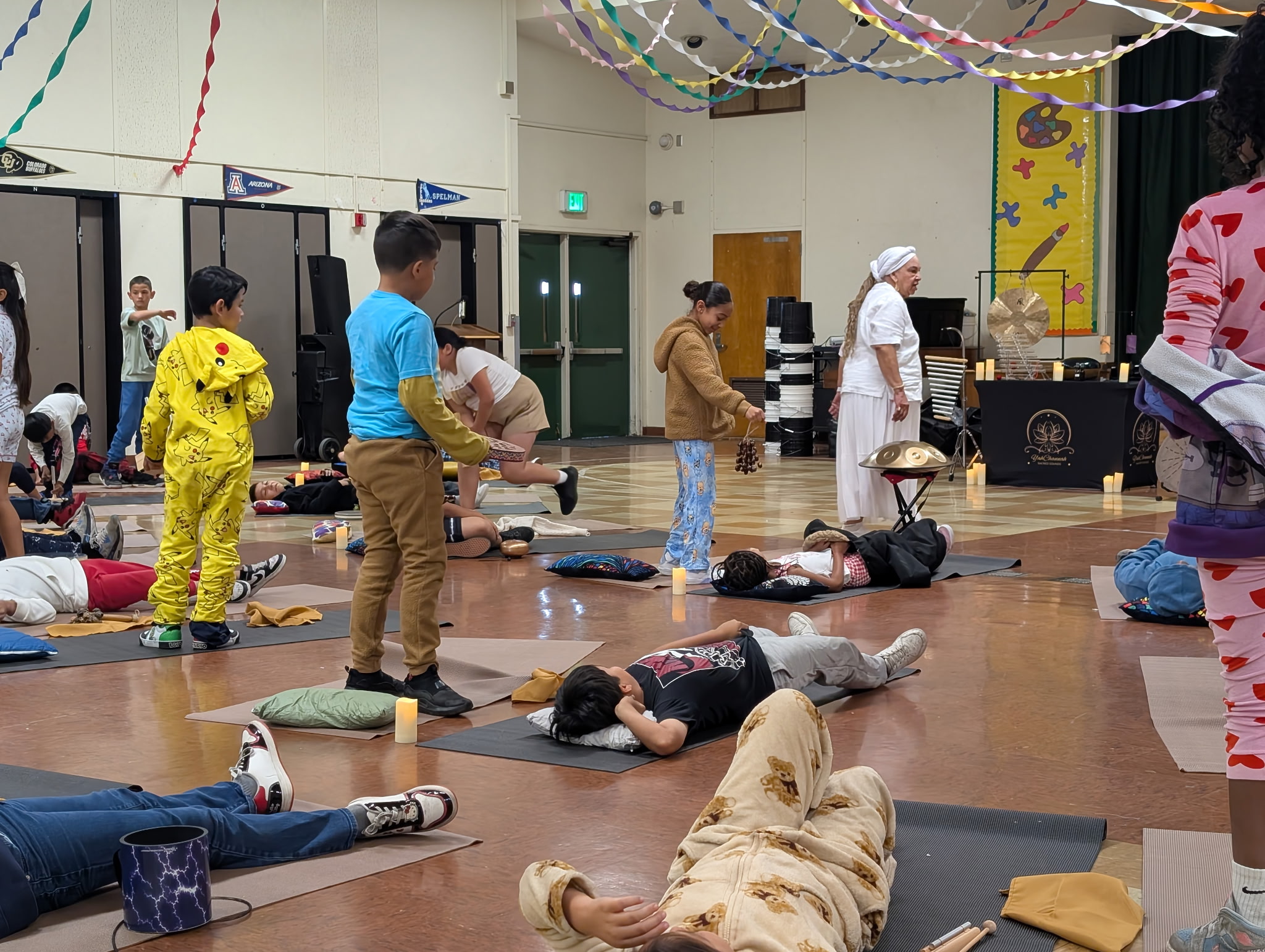 People lying on the floor and standing in a decorated indoor space, some in costumes, with others observing or assisting.