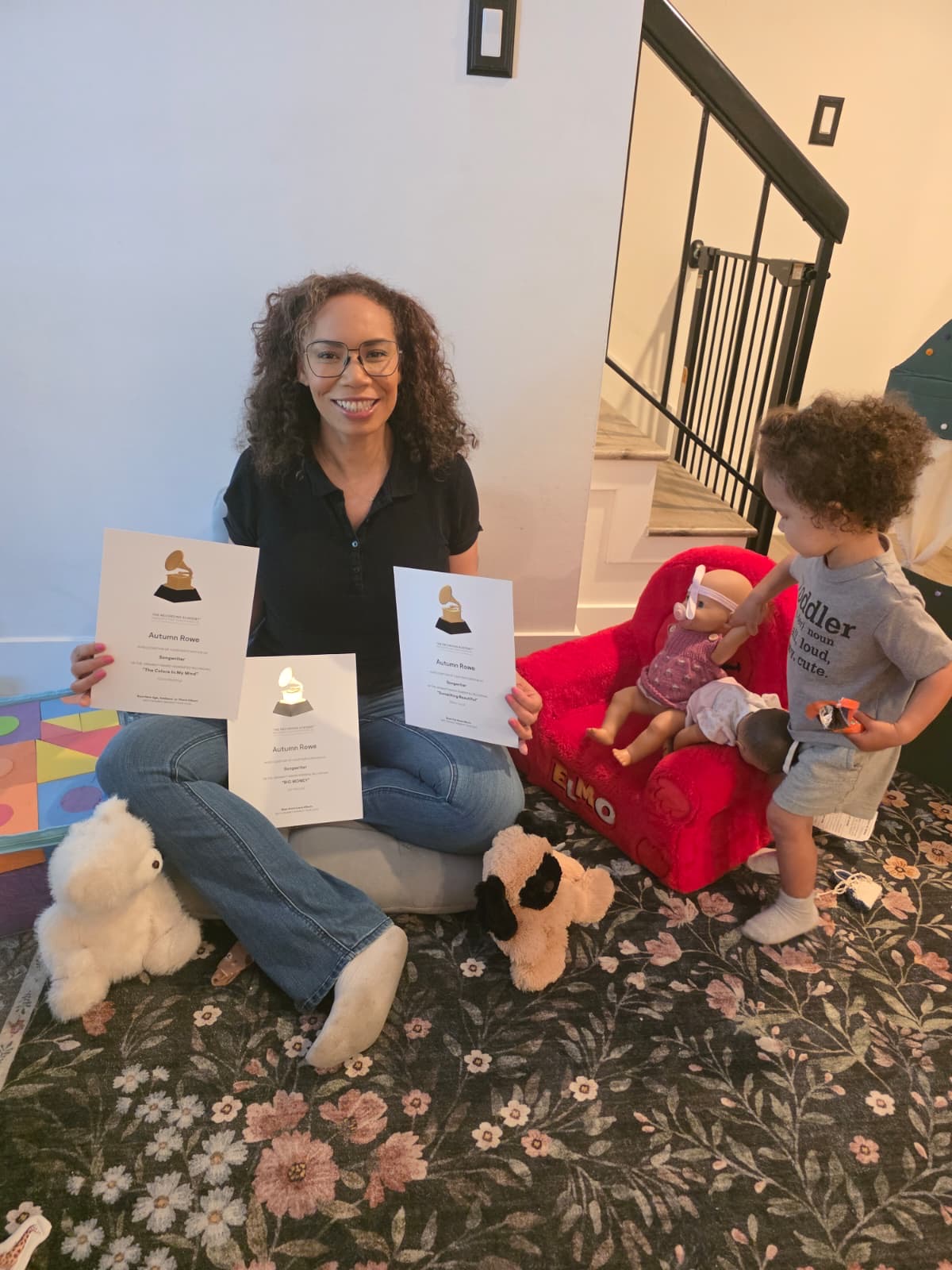 Woman sitting on the floor with children, surrounded by toys and books, in a home setting with stairs in background.