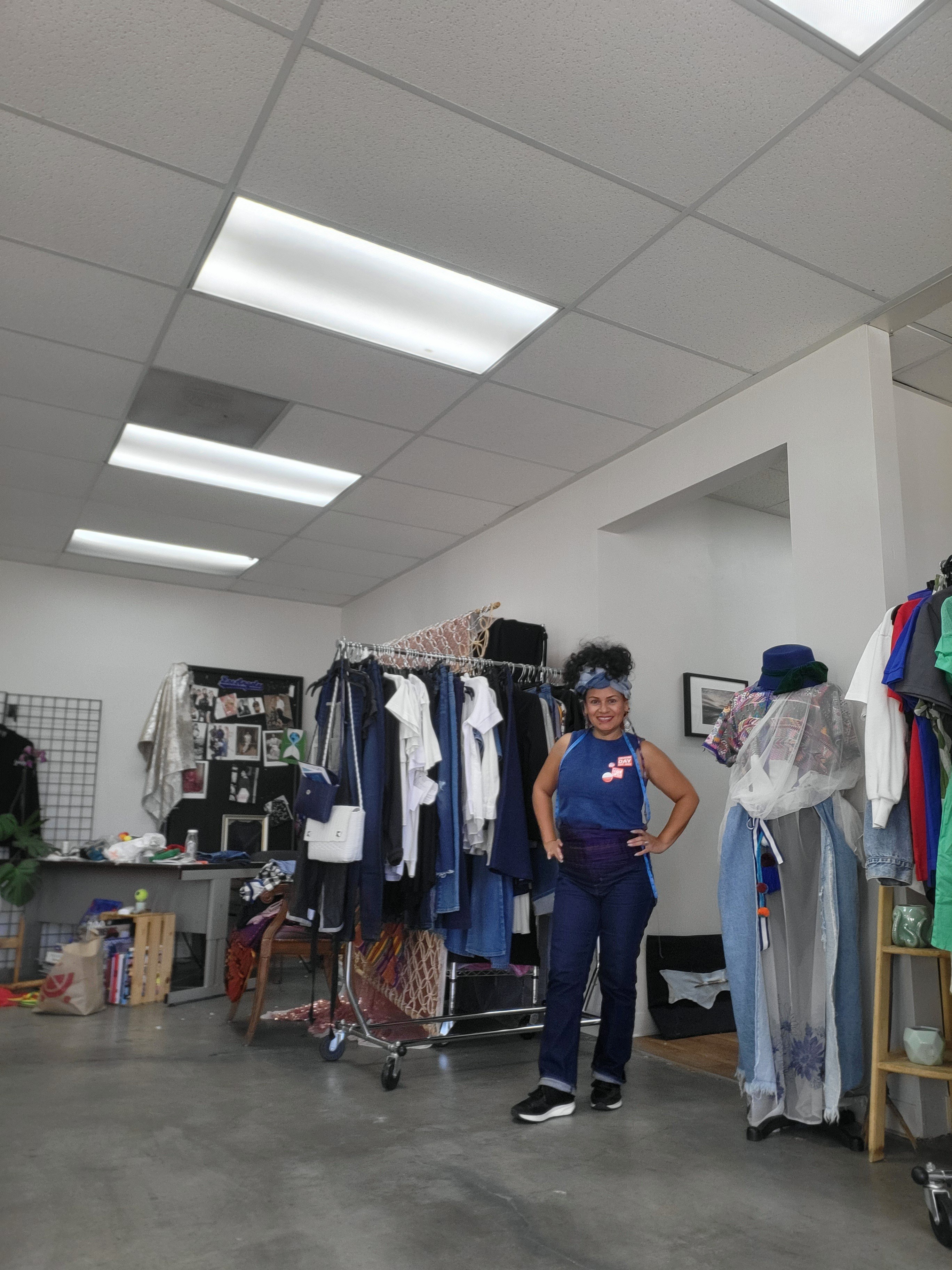 Person standing in a clothing store with racks of clothes and accessories, white walls, and ceiling lights.