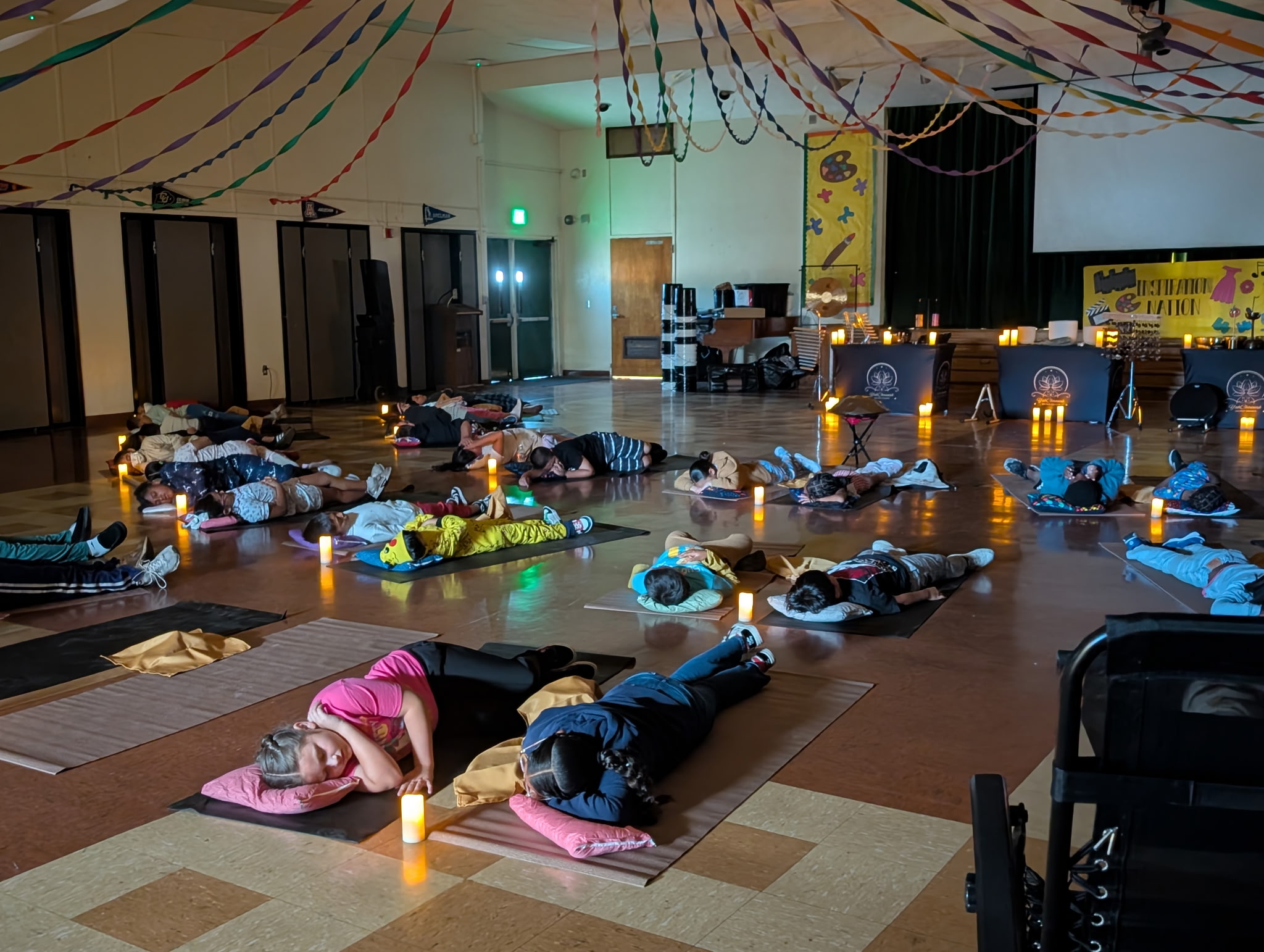 People lying on mats in a large room decorated with streamers, candles, and a stage in the background.