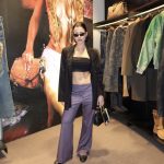 Woman in black crop top, striped pants, black jacket, sunglasses, holding a handbag, standing in clothing store.