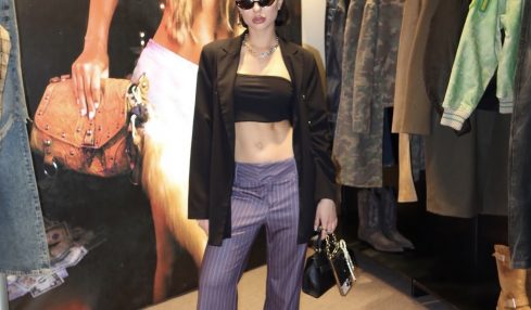 Woman in black crop top, striped pants, black jacket, sunglasses, holding a handbag, standing in clothing store.