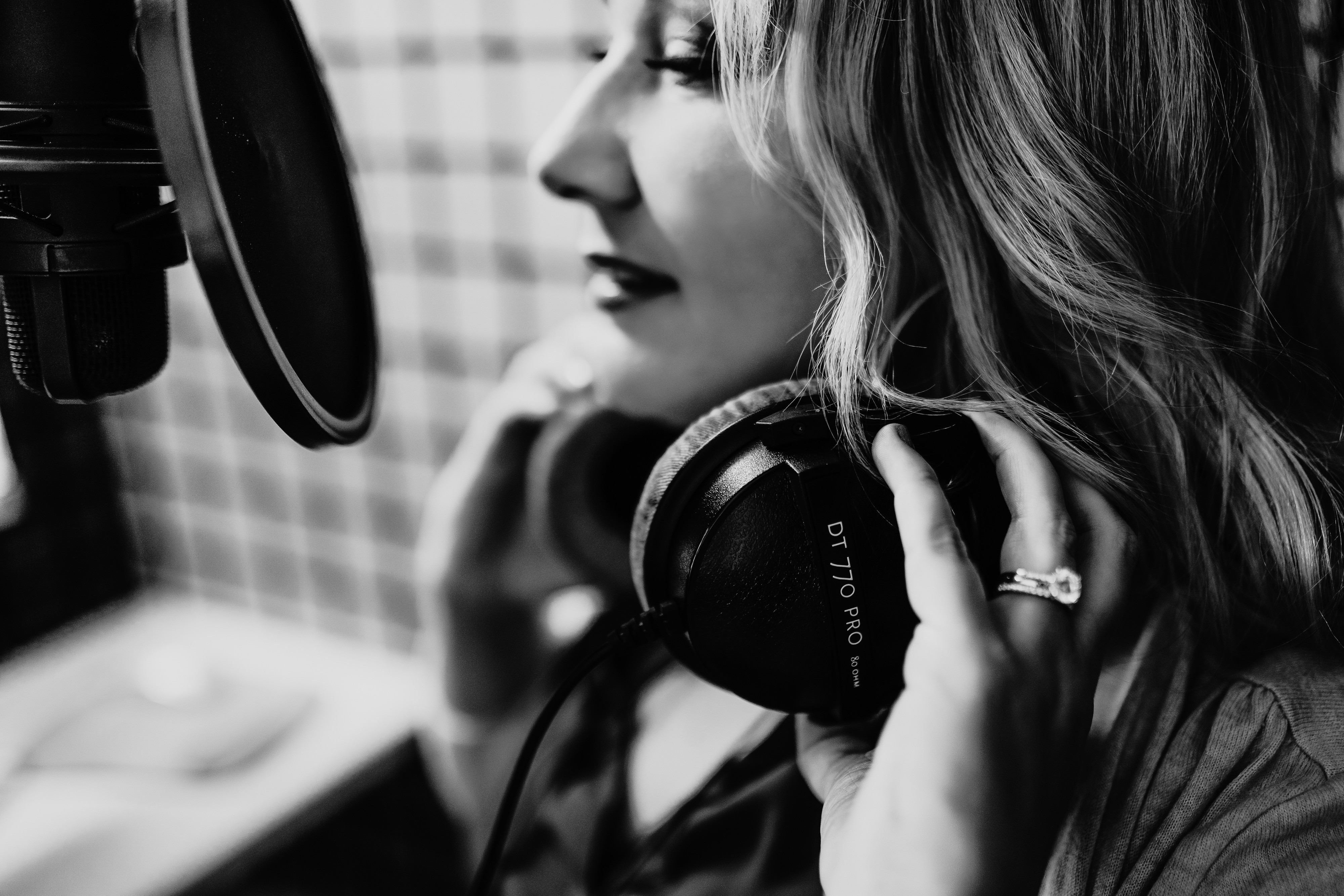 Woman with headphones in a recording studio, speaking into a microphone, with a blurred background.