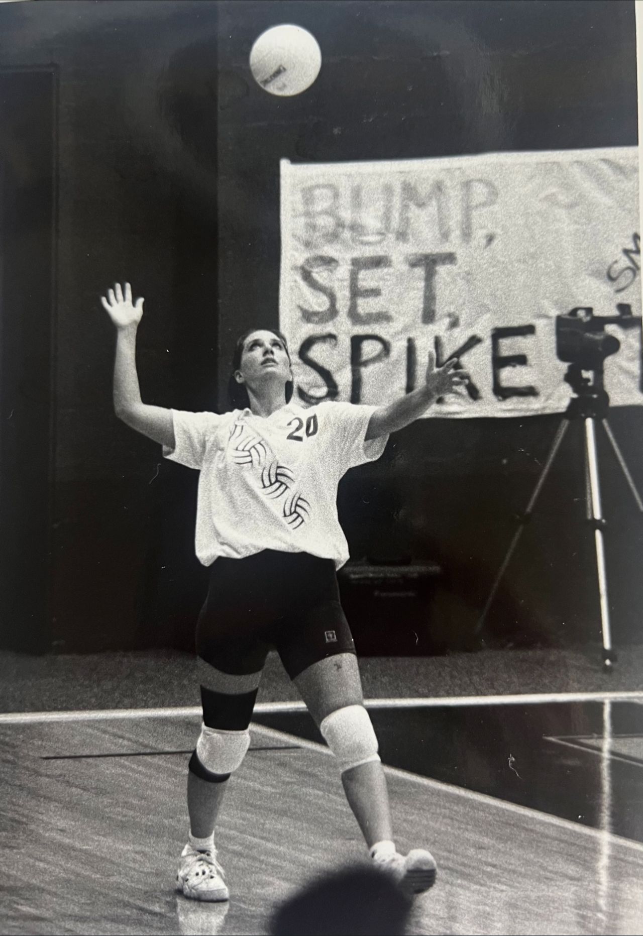 A volleyball player prepares to serve on court, with a banner reading 'BUMP, SET, SPIKE' in the background.