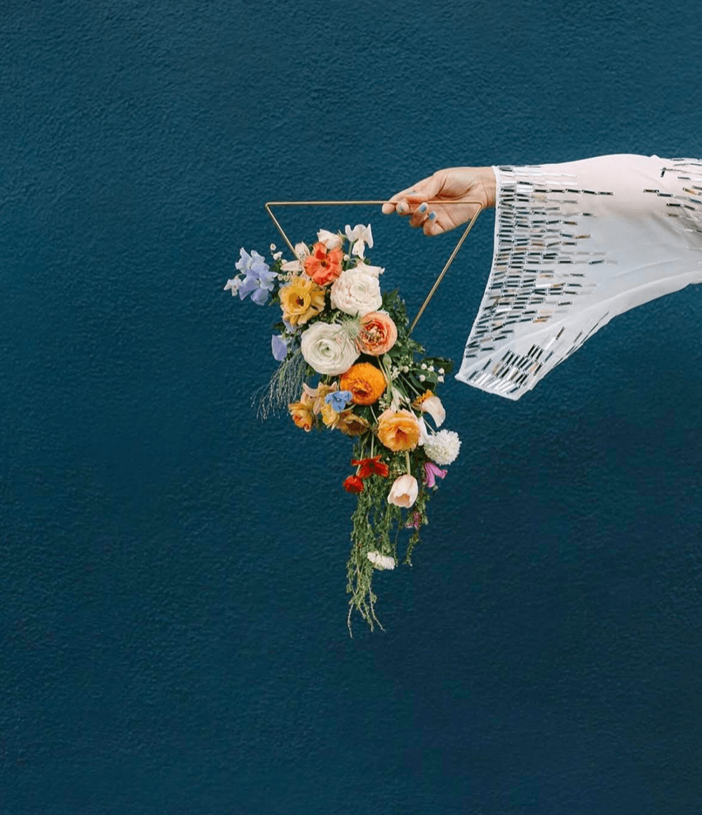 Person holding a colorful flower bouquet against a dark blue background, wearing a white patterned sleeve.