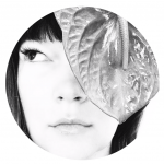 Close-up of a woman's face with a large leaf covering part of her face, black and white, circular crop.