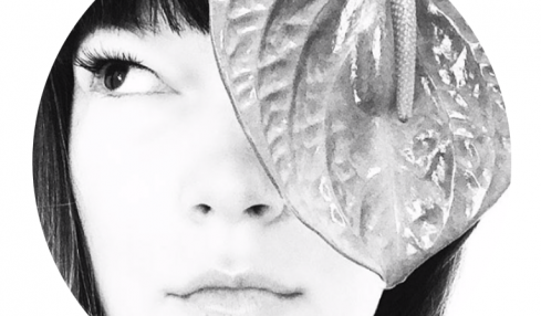 Close-up of a woman's face with a large leaf covering part of her face, black and white, circular crop.