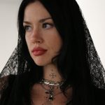 Woman with long black hair wearing black lace veil and jewelry, looking to the side, indoors.