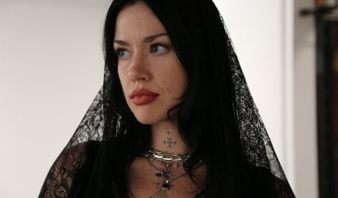 Woman with long black hair wearing black lace veil and jewelry, looking to the side, indoors.