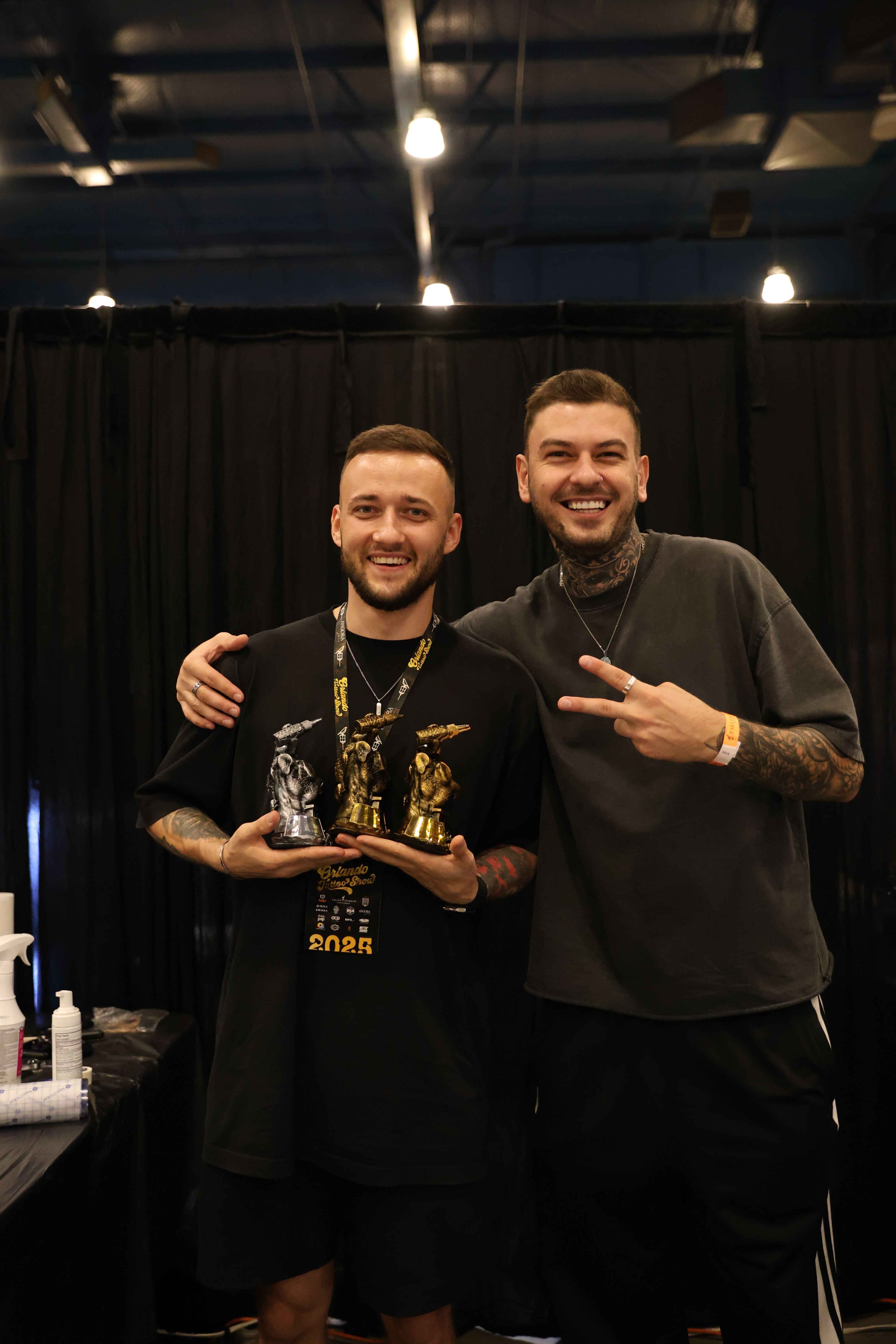Two men standing together, one holding an award, in front of a black curtain, smiling at the camera.