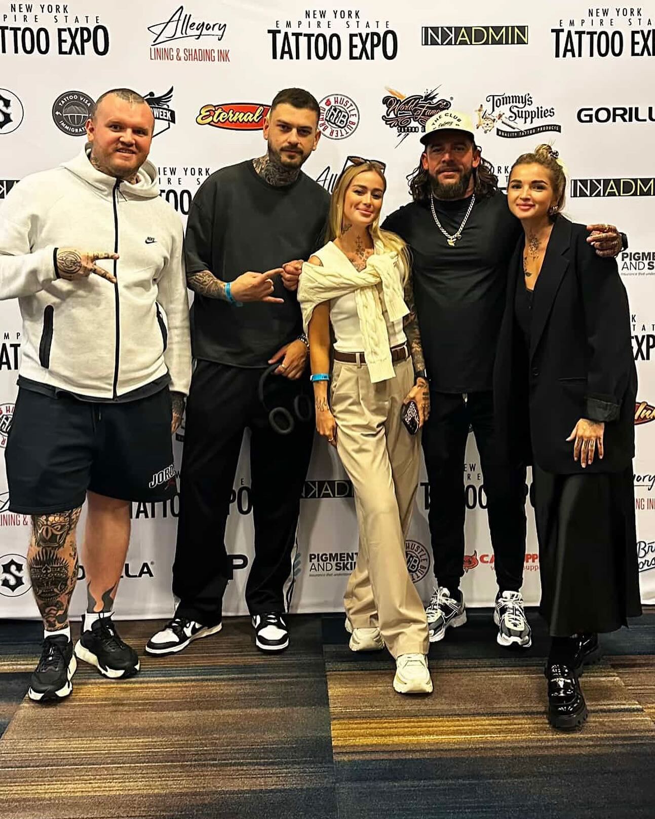 Group of five people standing together at a tattoo expo, smiling, with a backdrop displaying various logos and event names.