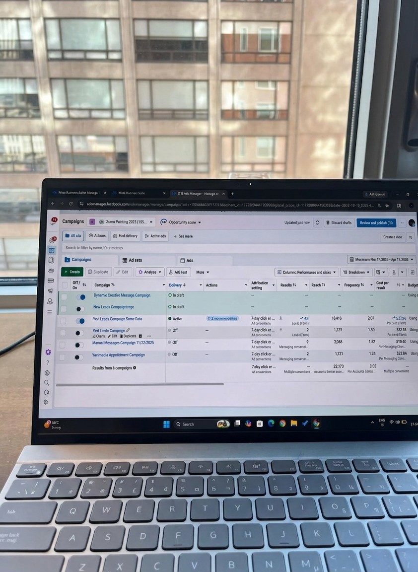 Laptop on a desk with a spreadsheet open, window with a building view in the background.