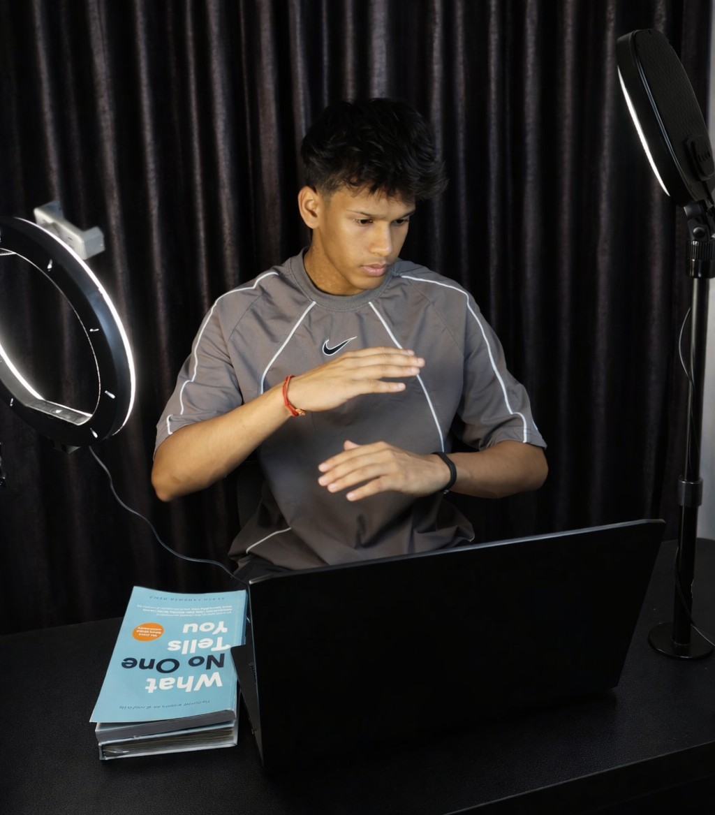Young person with dark hair wearing a gray Nike shirt, working on a laptop with studio lights and a black curtain background.