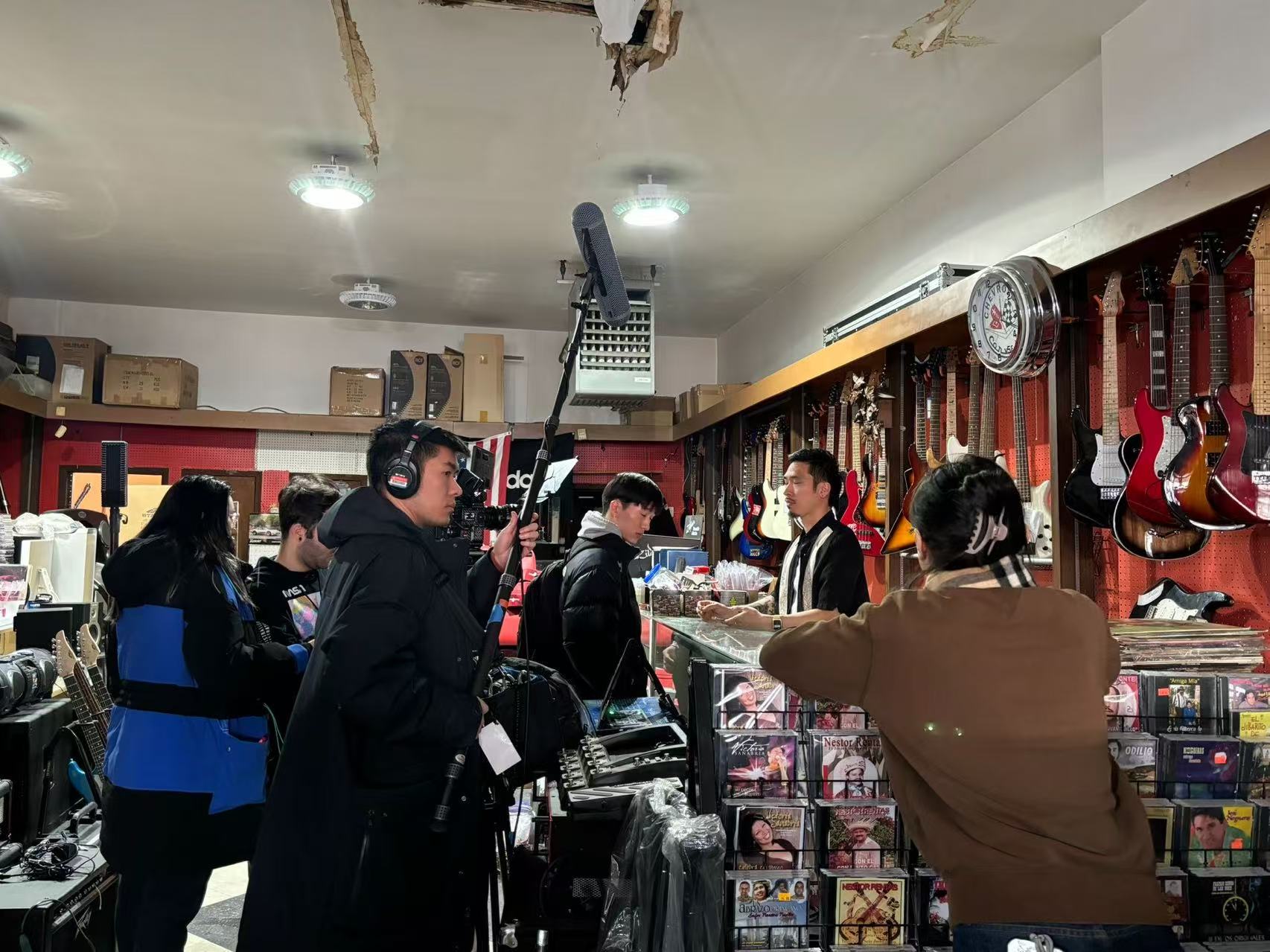 People inside a music store with guitars hanging on the wall, some browsing and others working behind the counter.