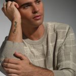 Young man with short dark hair, wearing a beige striped sweater, resting his head on his hand, looking thoughtful.