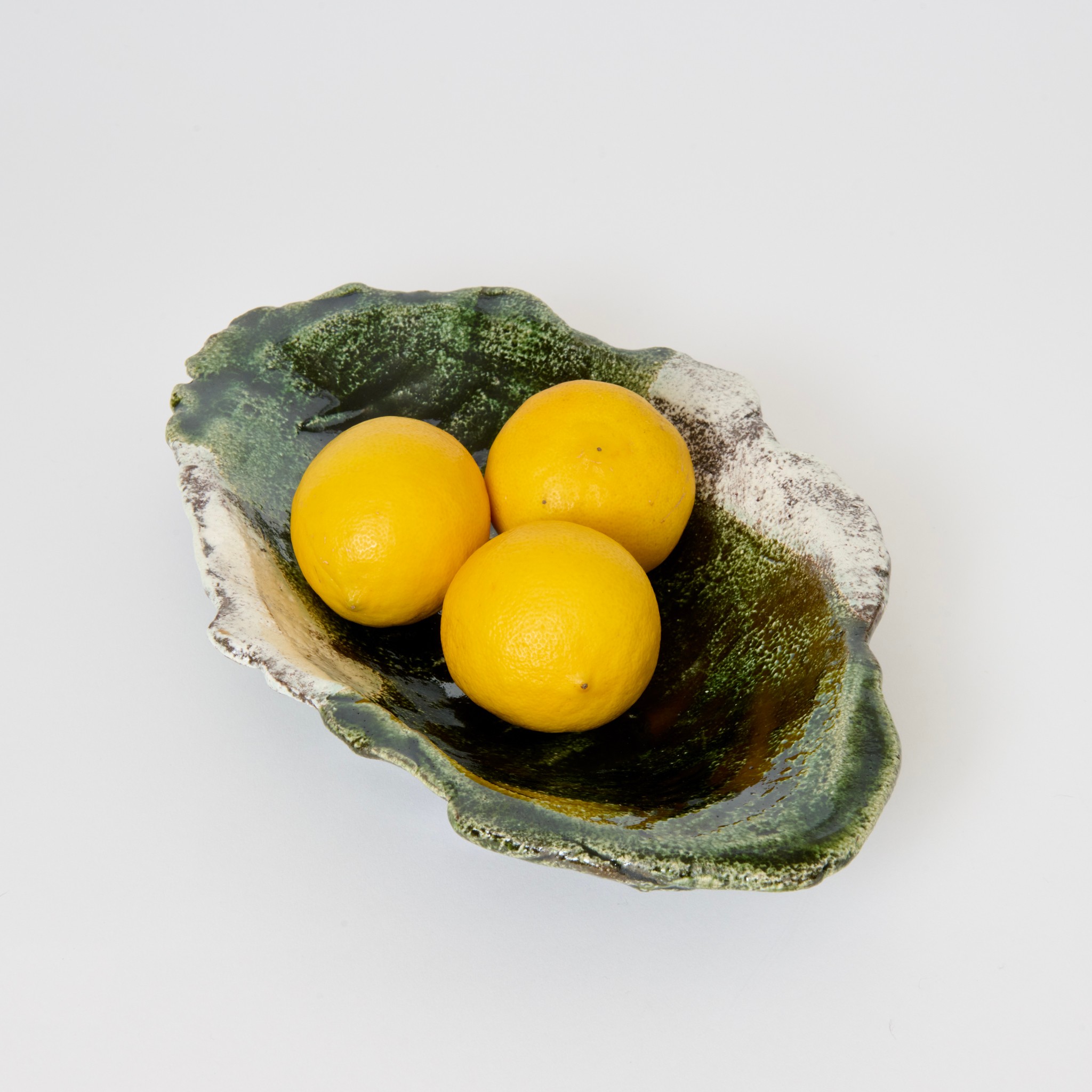 Three yellow lemons on a decorative green and brown ceramic dish, on a white background.