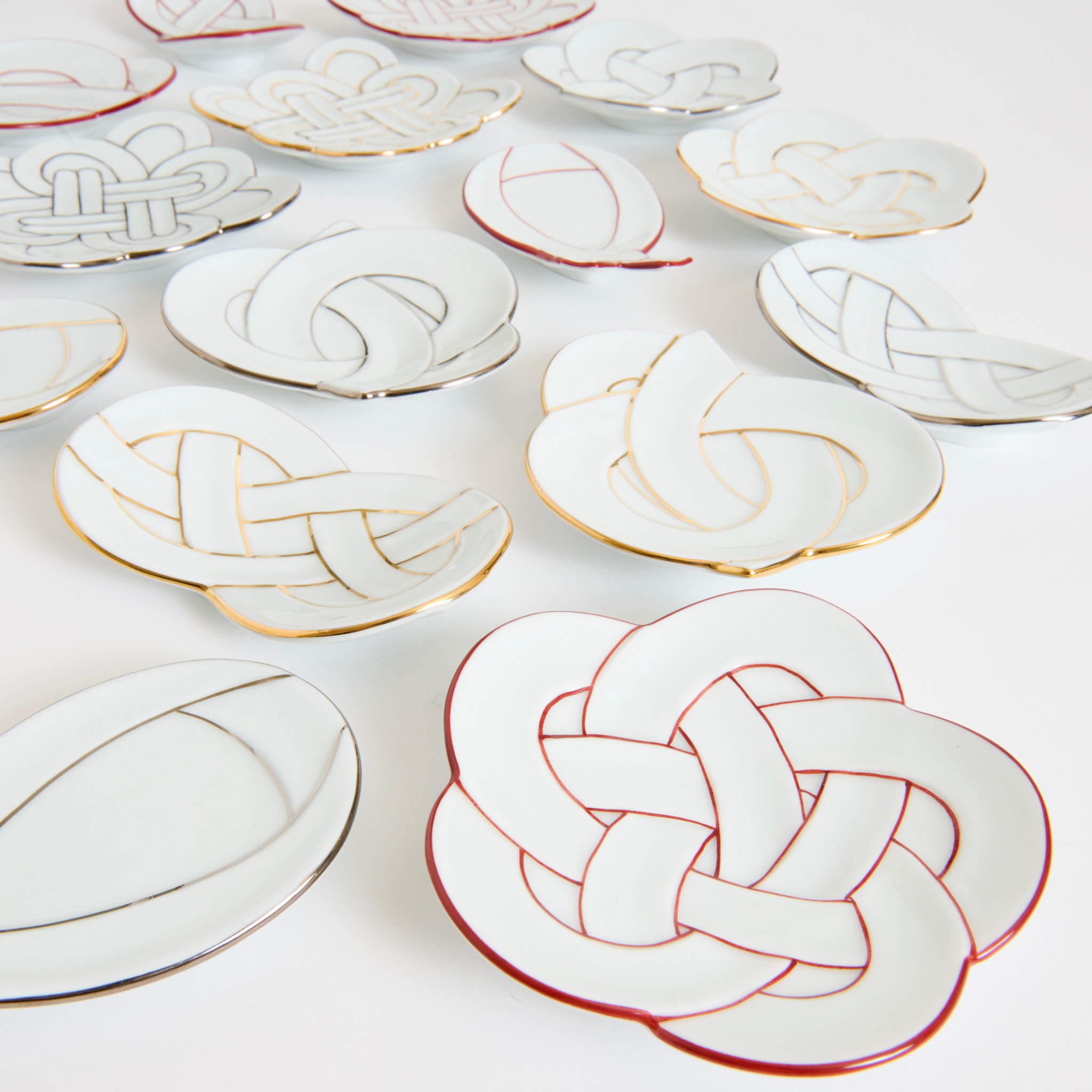 Decorative ceramic plates with intricate knot designs, some with gold and red accents, arranged on a white surface.
