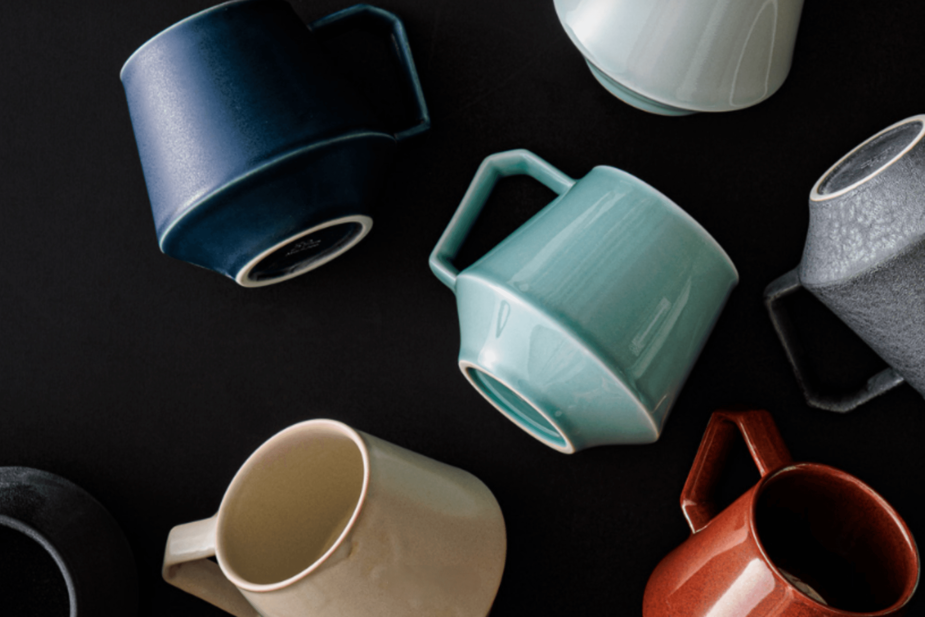 Various mugs and cups arranged on a dark surface, some tilted or upside down.