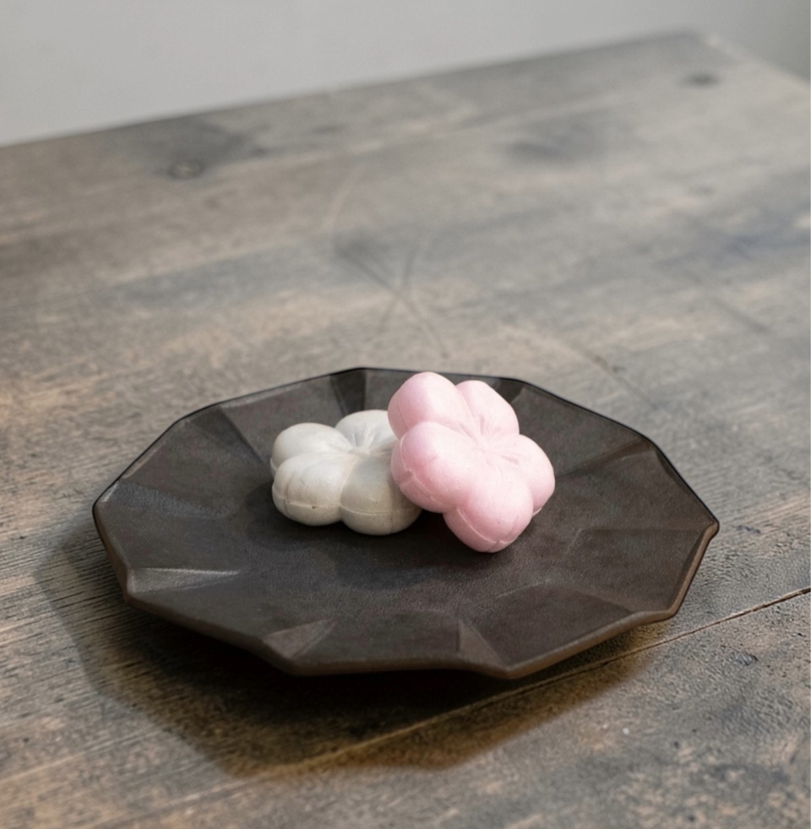 Two cloud-shaped objects, one white and one pink, on a dark plate on a wooden surface.