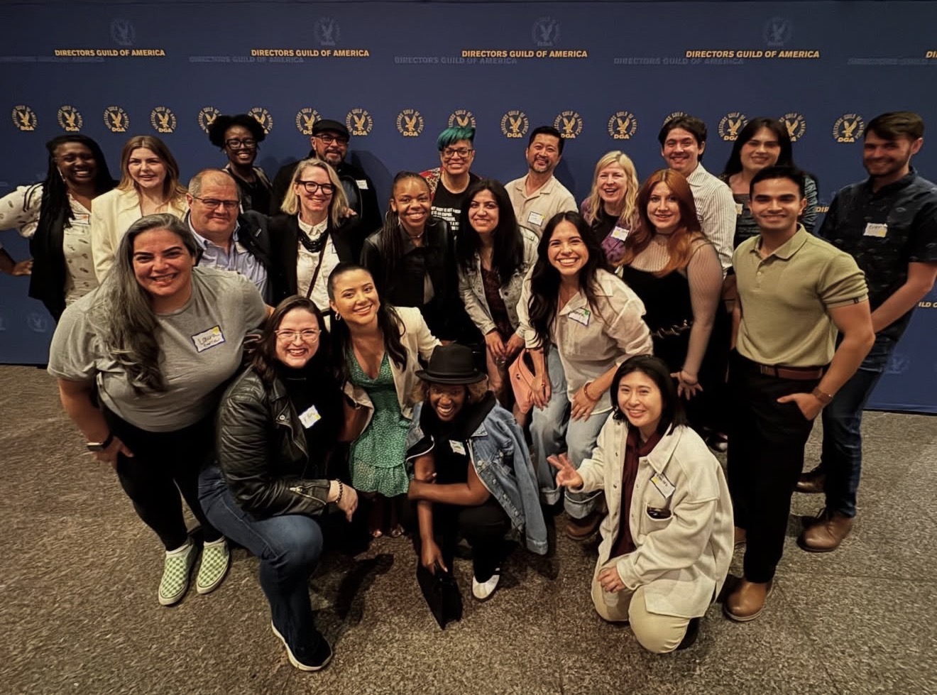 Group of diverse people smiling and posing together in front of a blue backdrop with logos and text.