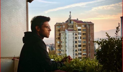 Person sitting at a balcony with a cityscape and mountains in the background during sunset