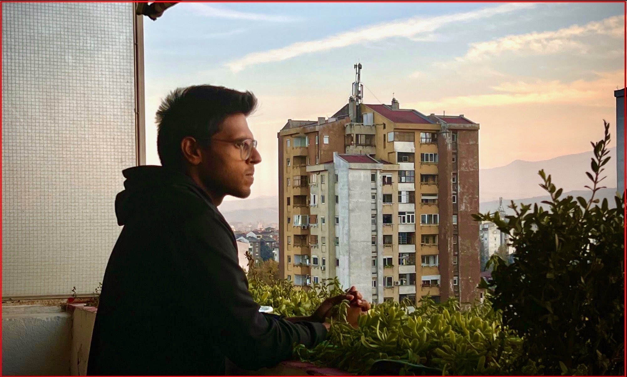 Person sitting at a balcony with a cityscape and mountains in the background during sunset