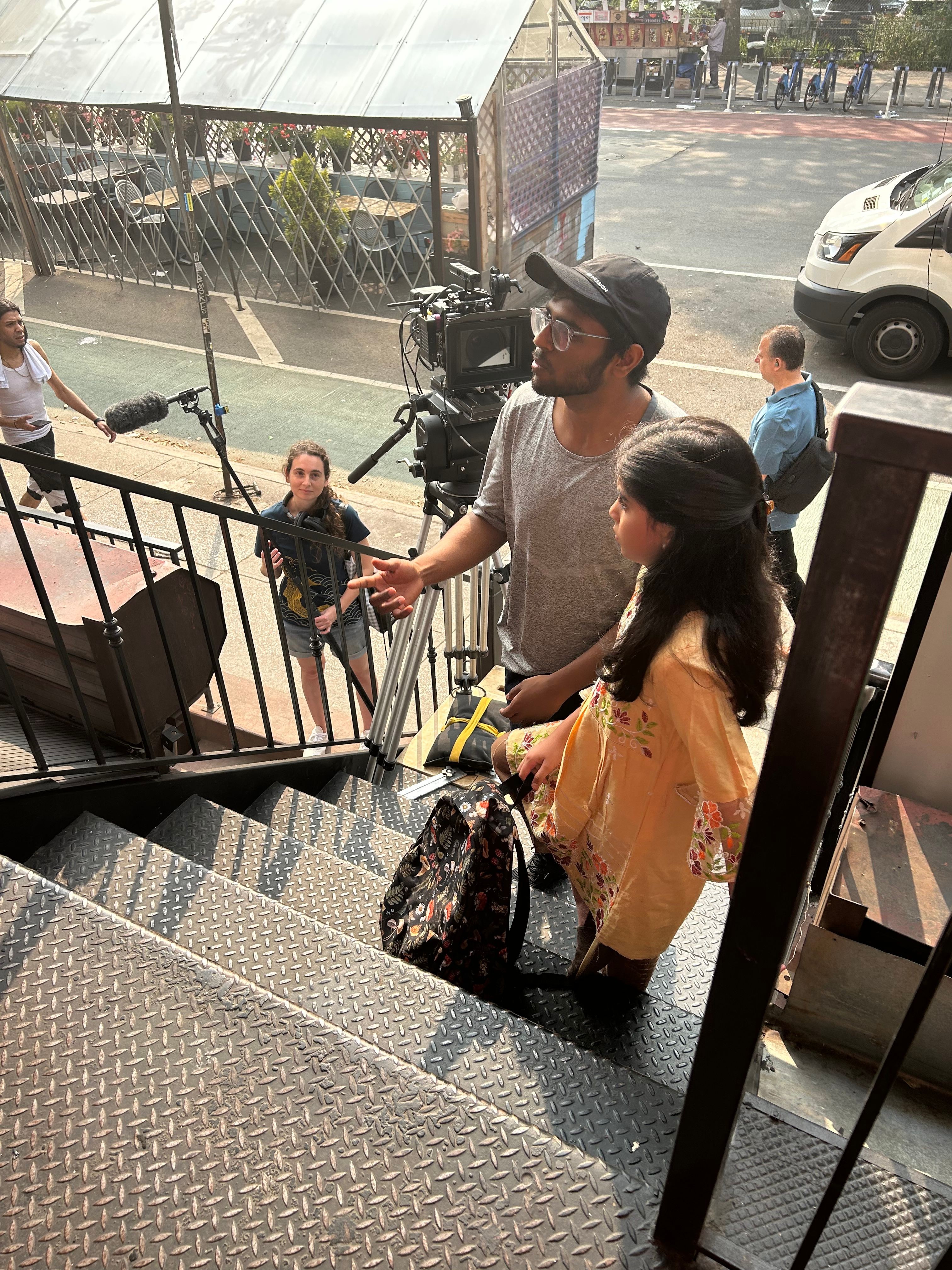 People standing on a sidewalk near a street with cars and buildings, some holding bags and talking.