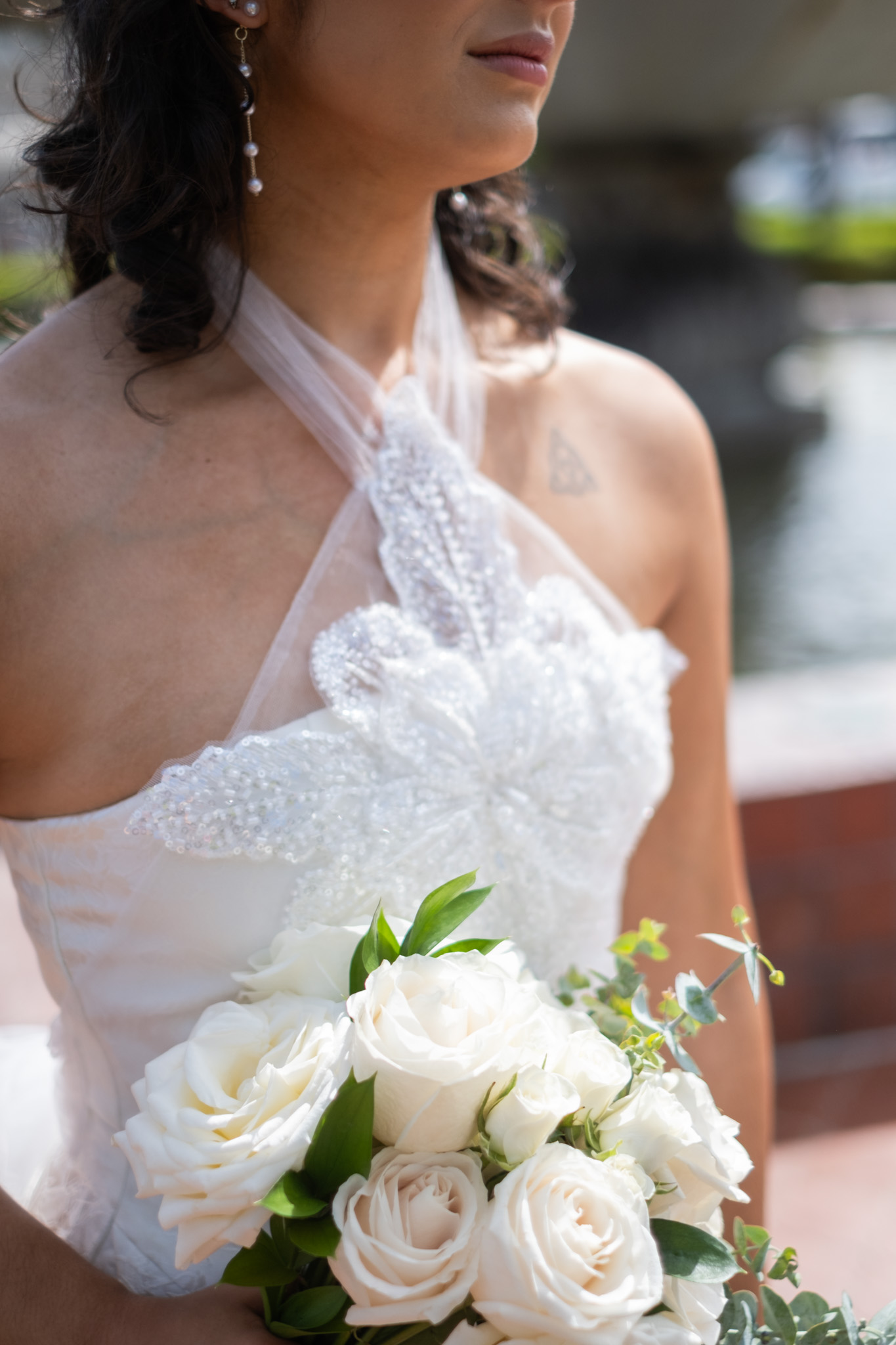 Woman in wedding dress holding a bouquet of white roses and greenery, outdoors near water.