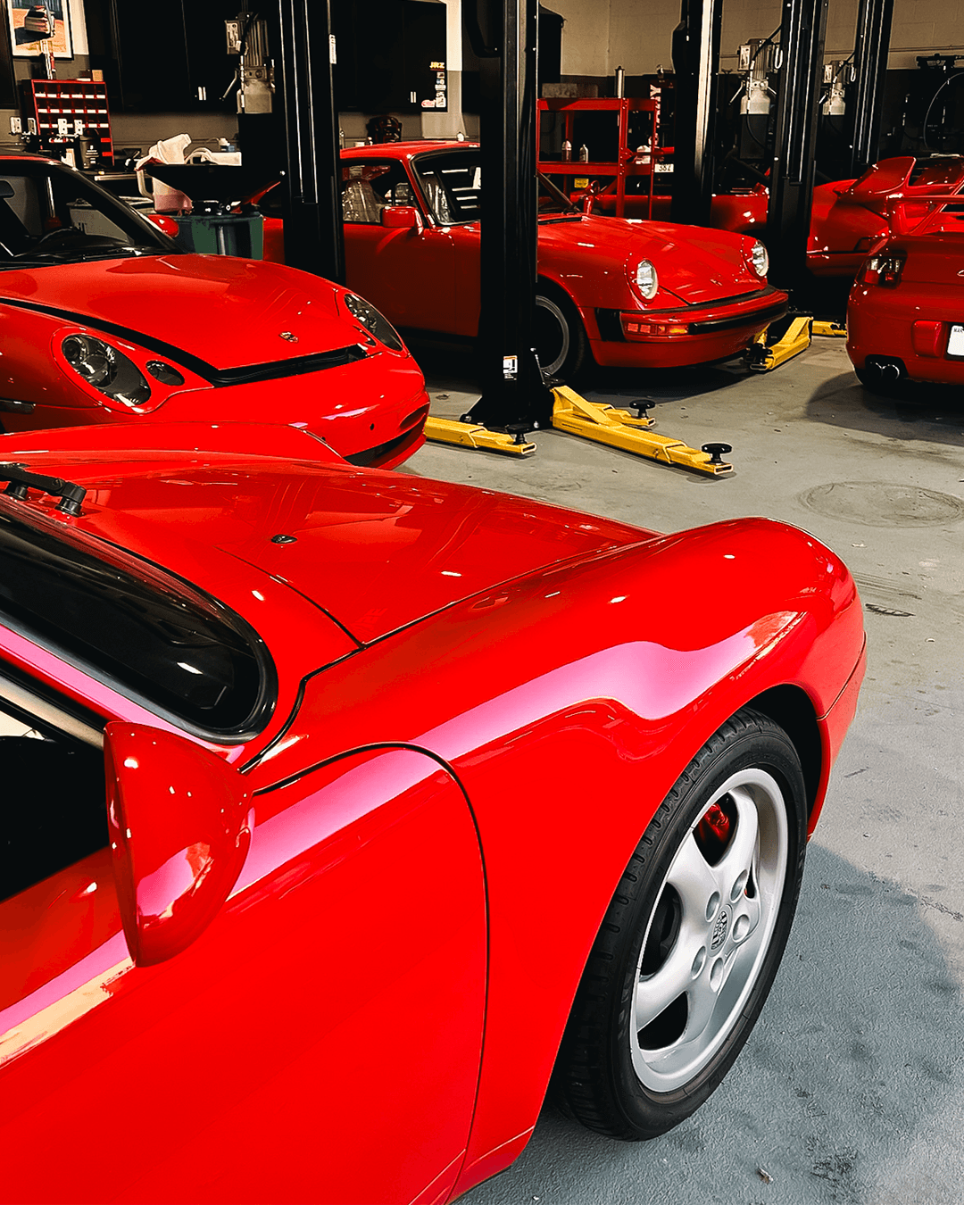 Multiple red sports cars parked in a garage, with one car prominently in the foreground showing its front and side.