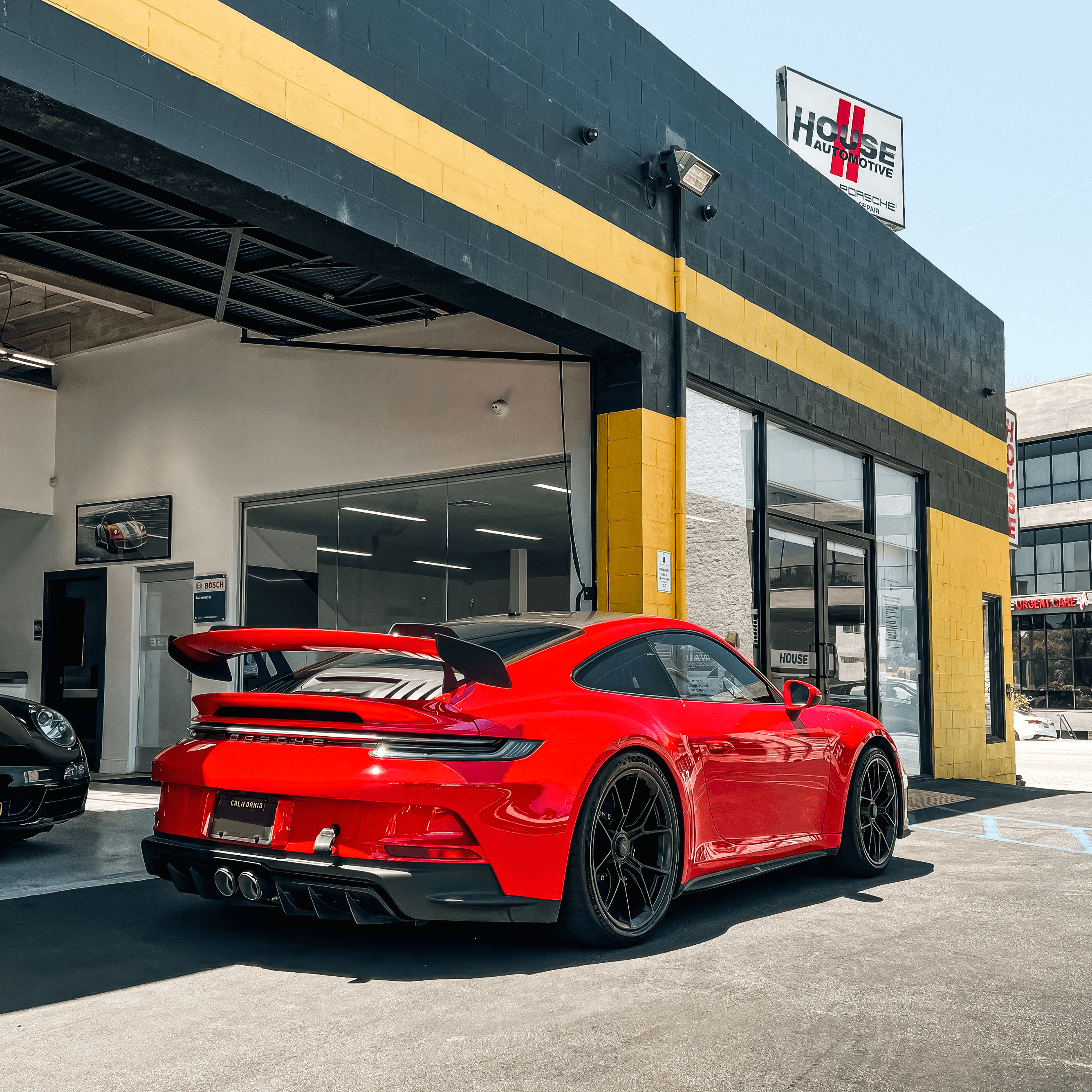 Red sports car with a large rear wing parked outside a black and yellow building with glass windows.