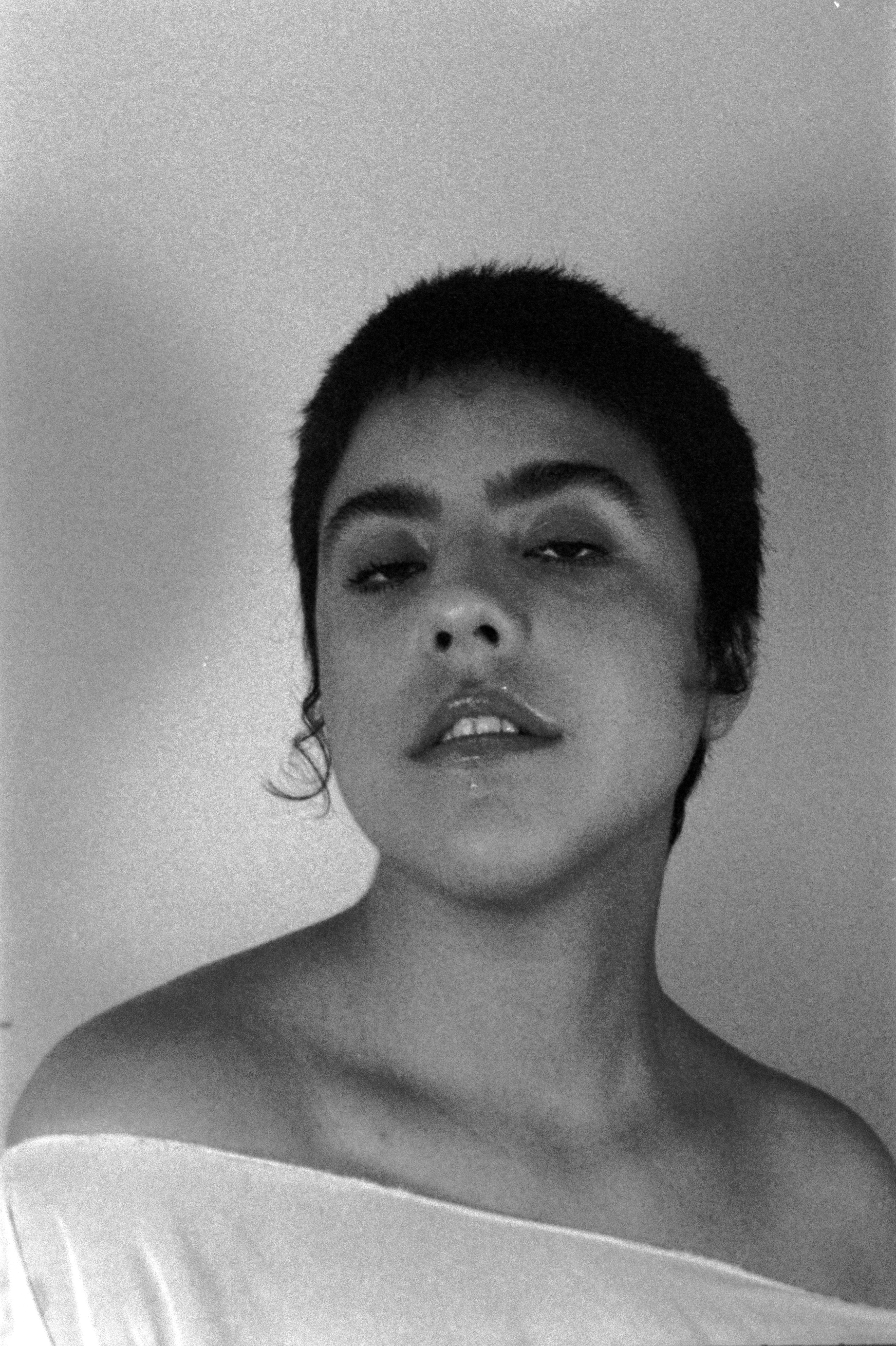 Portrait of a person with short hair, looking slightly to the side, wearing an off-shoulder top, in black and white.