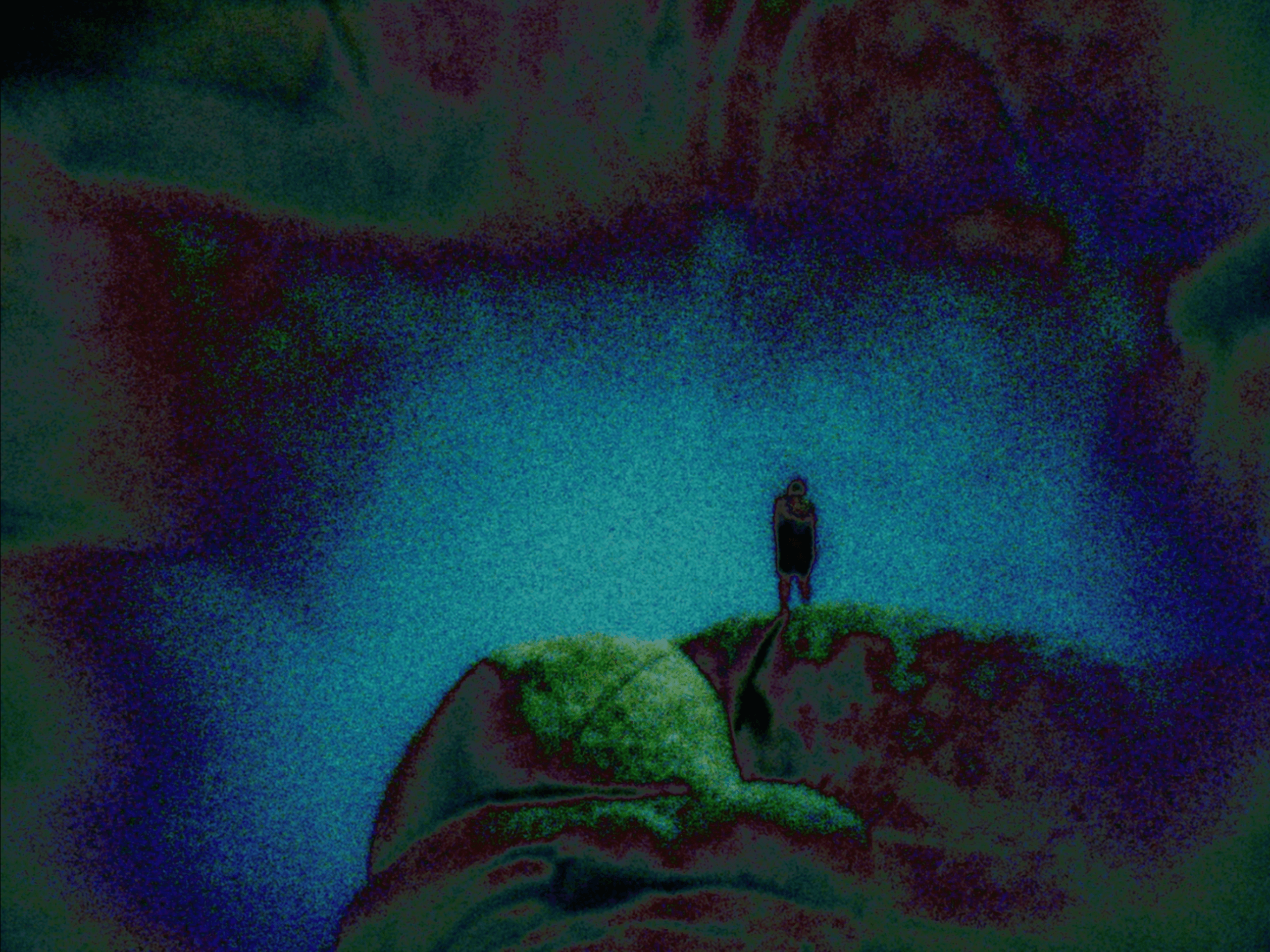Person standing on a rocky ledge overlooking a waterfall with colorful sky in background.