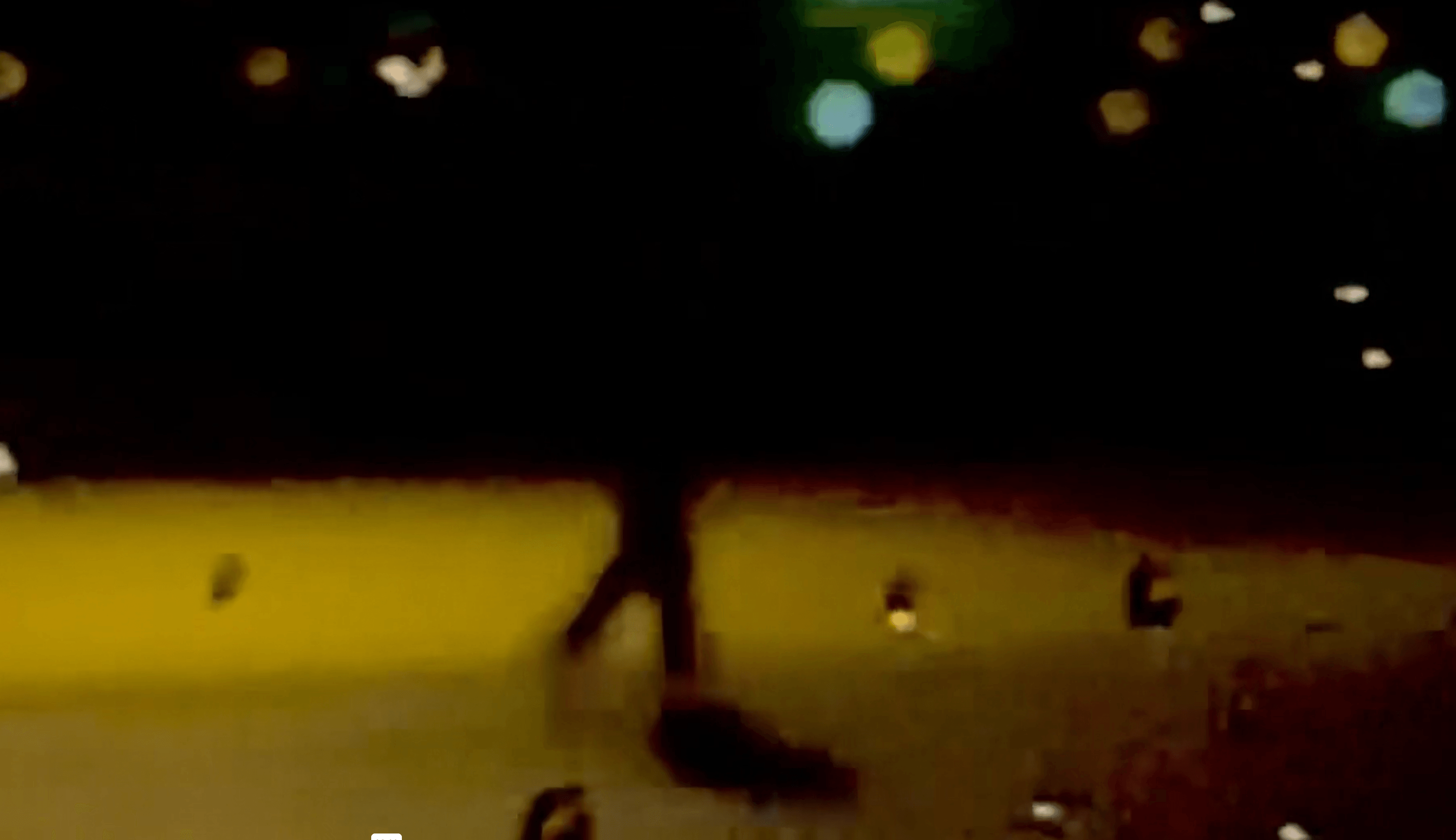 Person walking on a beach at night with blurred lights in the background.
