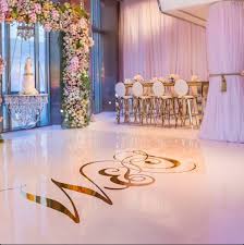 Elegant event space with floral arrangements, a cake, and a dance floor with a decorative message, in soft lighting.