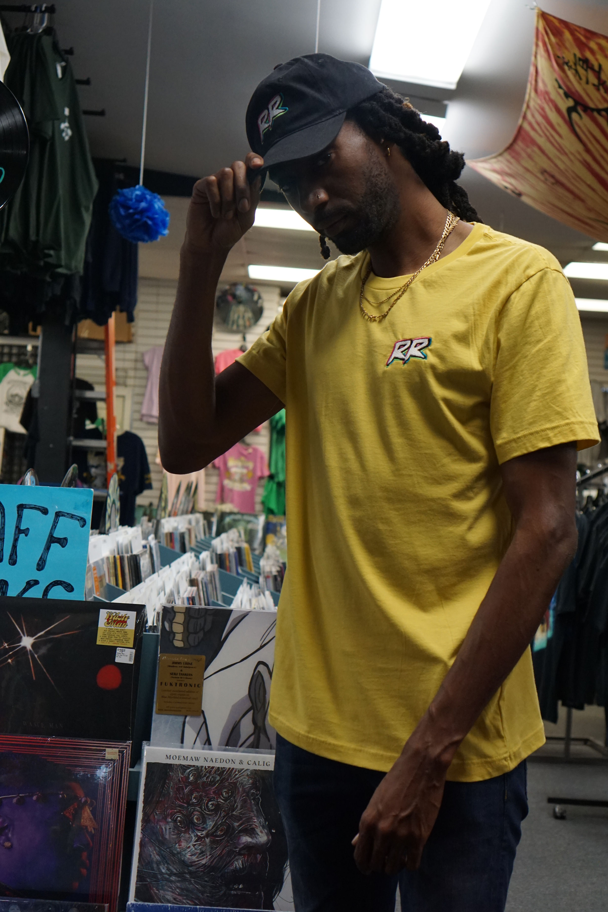 Person wearing a yellow T-shirt and cap, shopping in a store with clothing and accessories displayed.