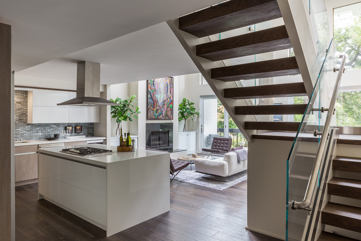 Open-concept living space with kitchen island, staircase, and seating area with large windows and plants.