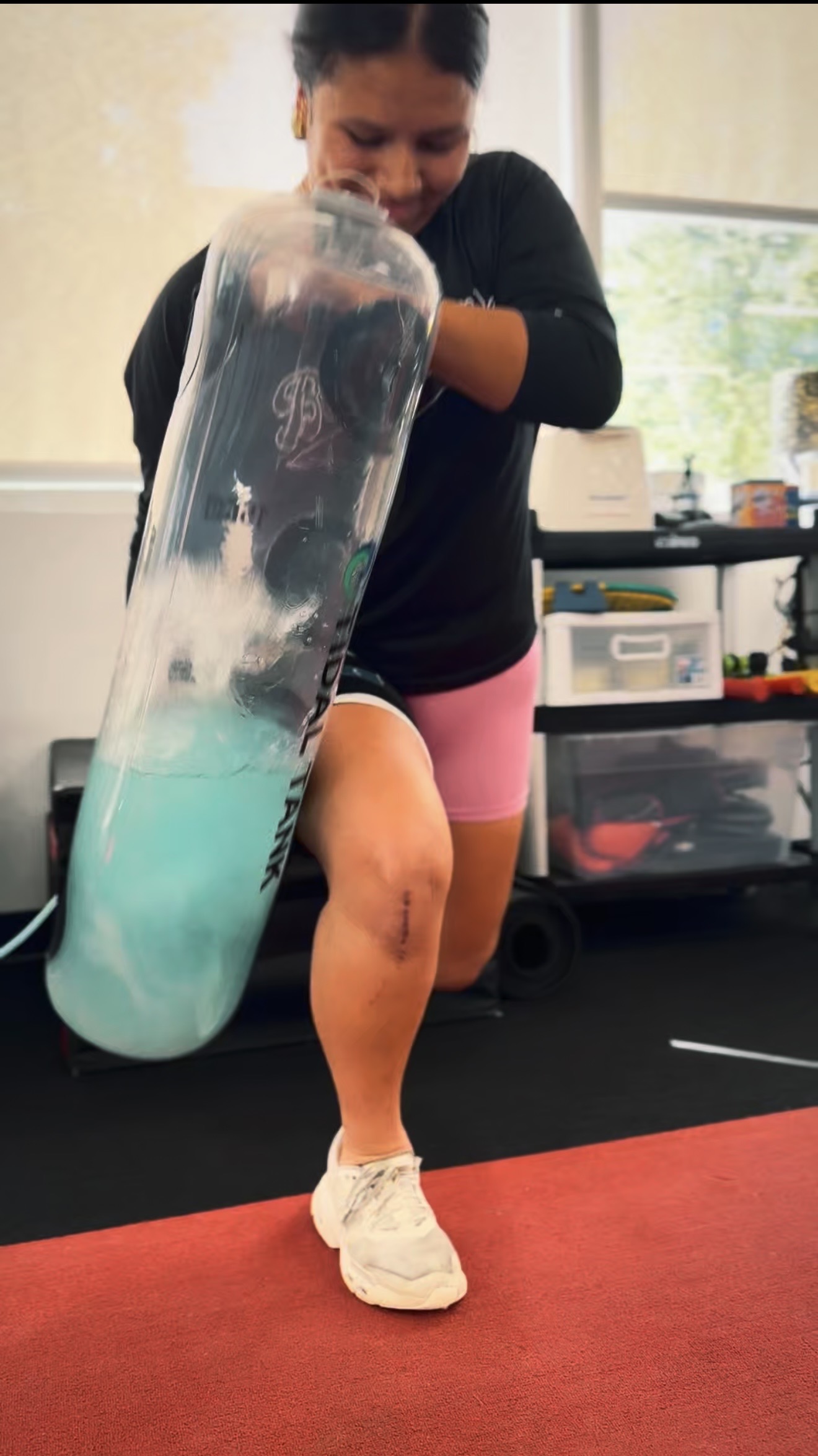 Person balancing on one leg while holding a large transparent container with blue liquid inside.