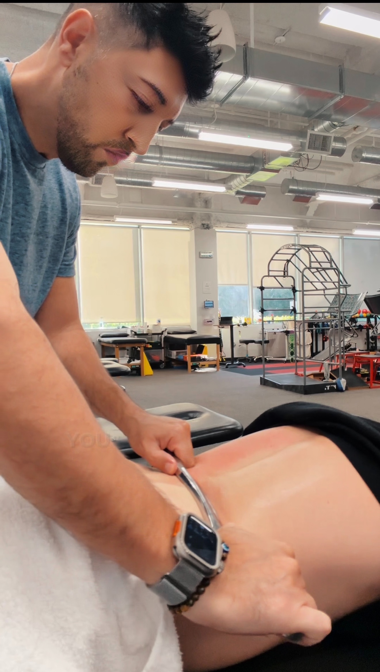 Person performing a medical procedure on a patient lying face down in a clinical setting.