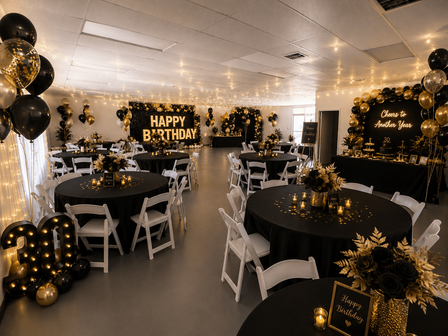 Celebration room decorated with black, gold, and white balloons, flowers, and birthday signs, with tables and chairs arranged for guests.