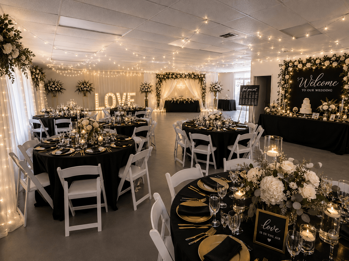 Wedding reception decorated with string lights, floral arrangements, and a welcome sign, with round tables and white chairs.
