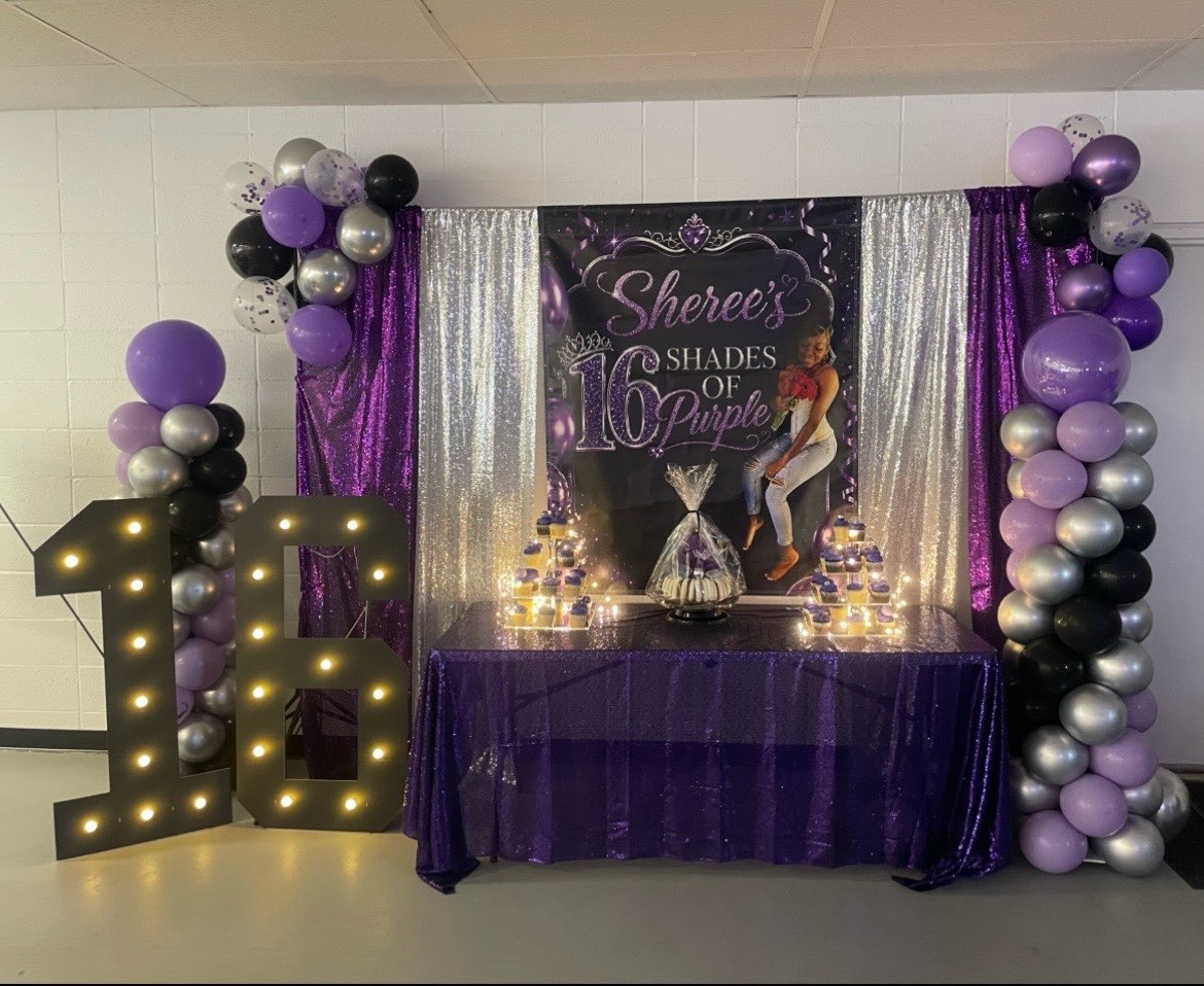 Party setup with purple, black, and silver balloons, a large illuminated number 16, and a decorated table with a themed backdrop.