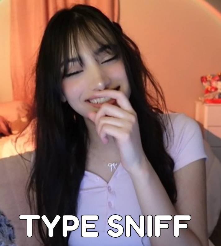 Young woman with long dark hair smiling and covering her mouth with her hand, in a softly lit room.