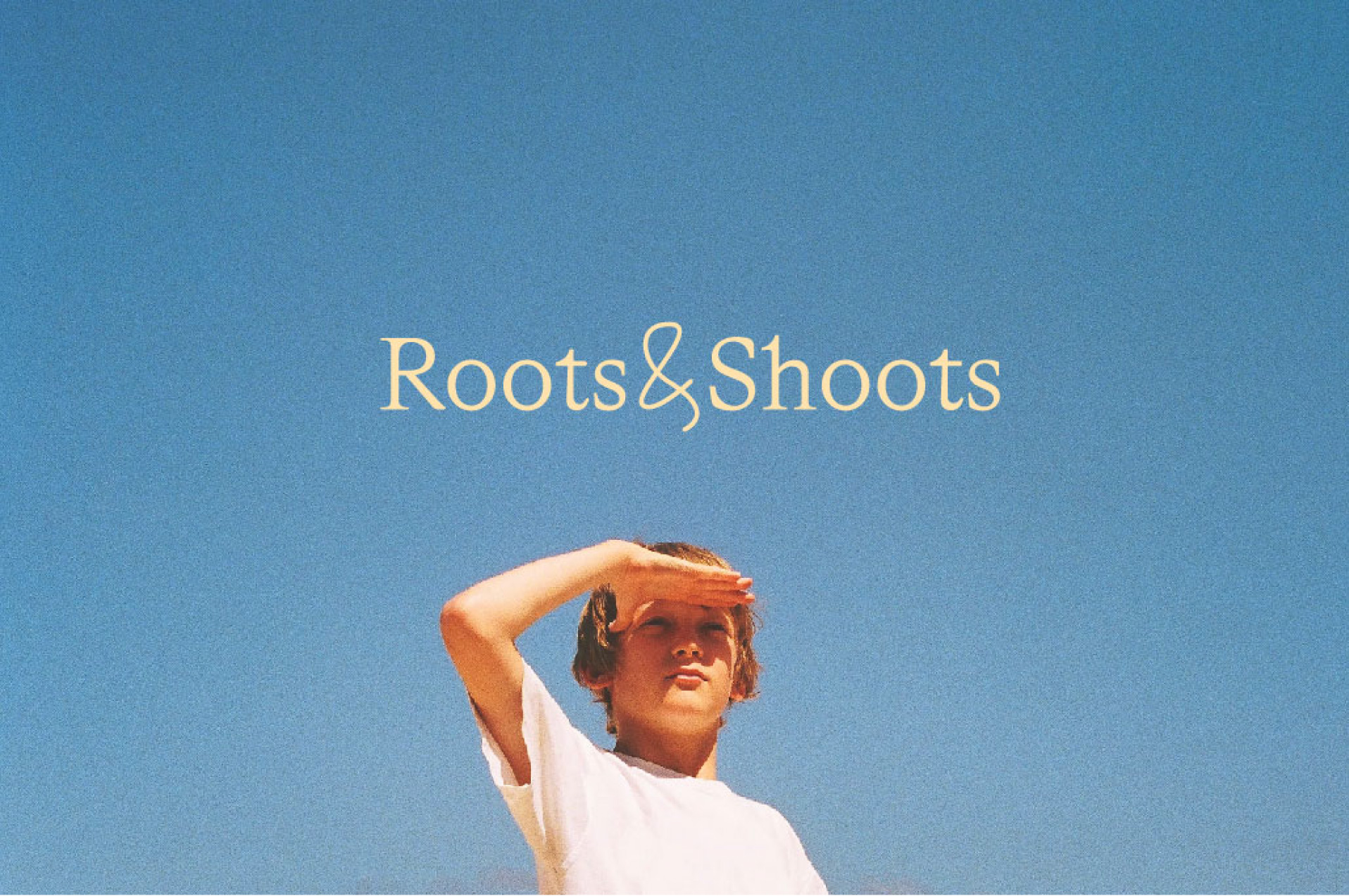 Person with short hair and white shirt shielding eyes against clear blue sky, text reads 'Roots&Shoots'.