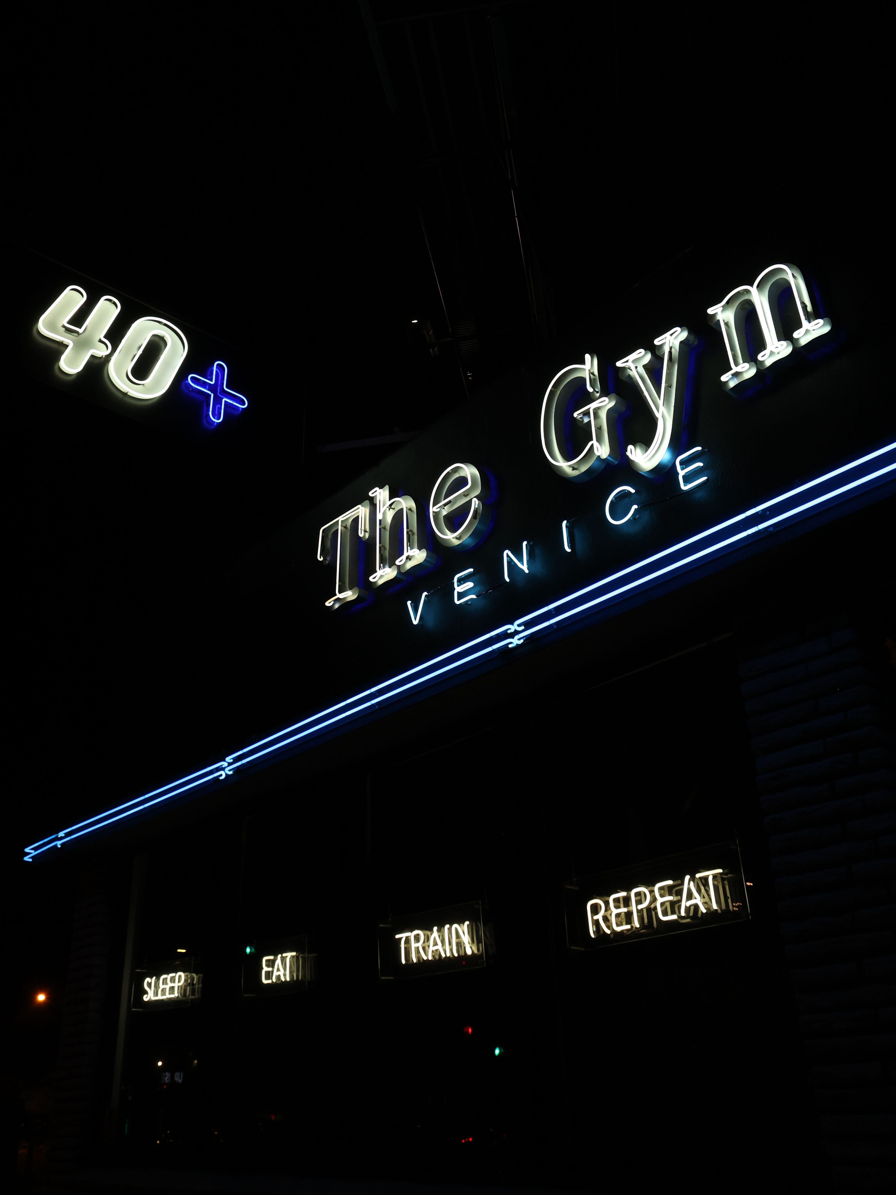 Neon sign for The Gym Venice with blue and white lights, and menu options on a dark background.